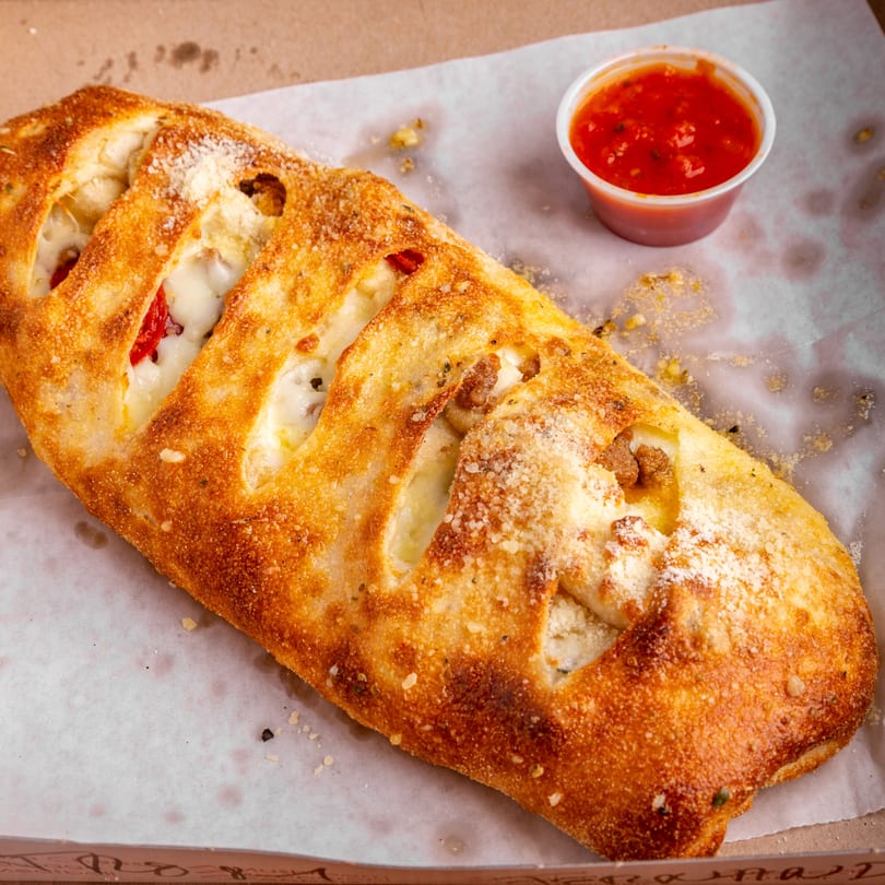 Golden-brown calzone with visible cheese and meat filling, served with a side of red marinara sauce.