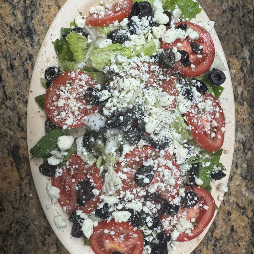 Overhead view of a Greek salad with lettuce, tomatoes, black olives, and feta cheese.